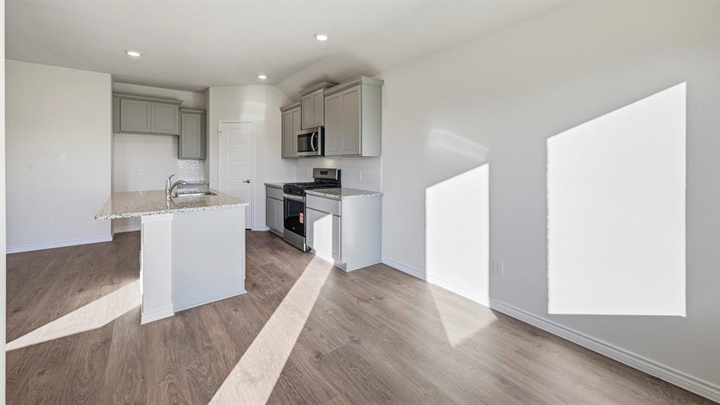419 Epiphany Lane Lavon, TX 75166 - Photo 2 of 31 Open-concept kitchen and living area featuring wood-finish flooring, recessed lighting, a kitchen island with an undermount sink, granite countertops, and stainless steel appliances
