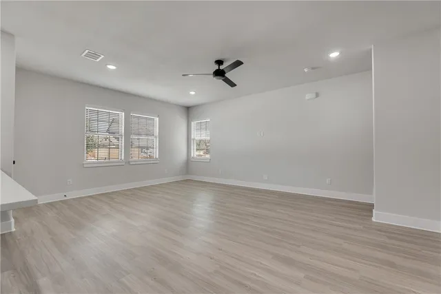 an empty room with wooden floor ceiling fan and windows