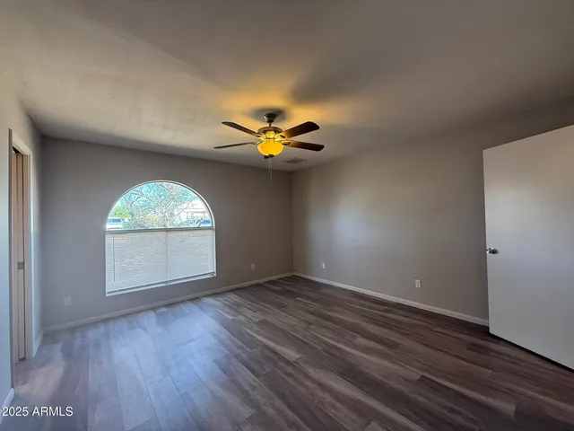 an empty room with wooden floor chandelier fan and windows