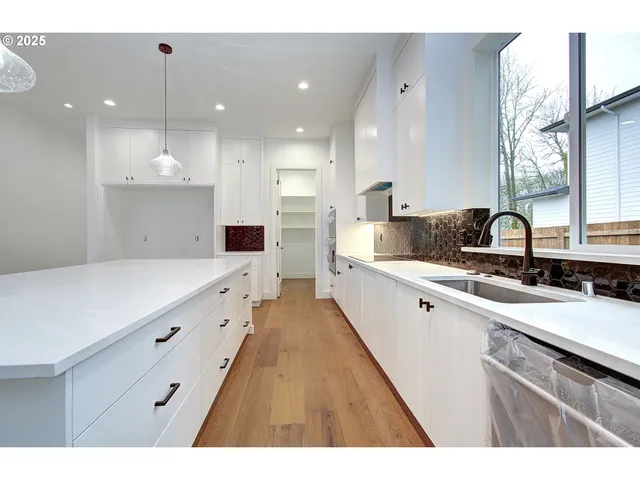 a large white kitchen with a large counter top a sink a window and stainless steel appliances