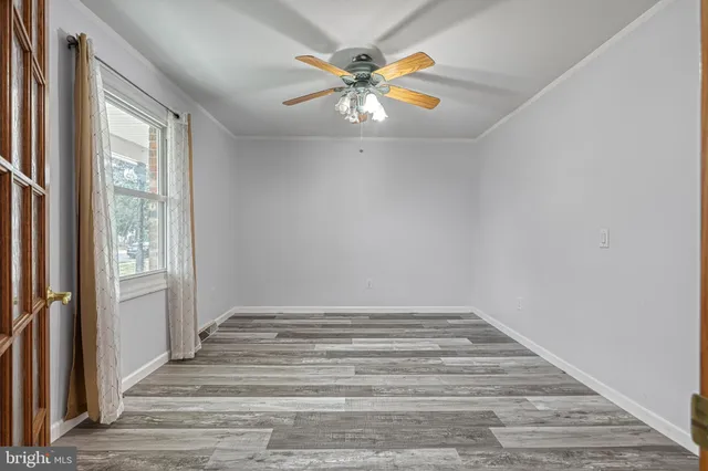 an empty room with wooden floor a ceiling fan and windows