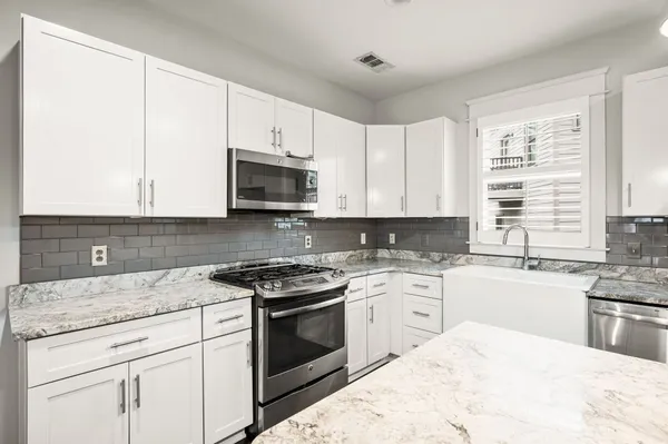 a kitchen with stainless steel appliances granite countertop white cabinets a sink a stove a microwave and wooden floors