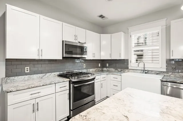 a kitchen with stainless steel appliances granite countertop white cabinets a sink a stove a microwave and wooden floors