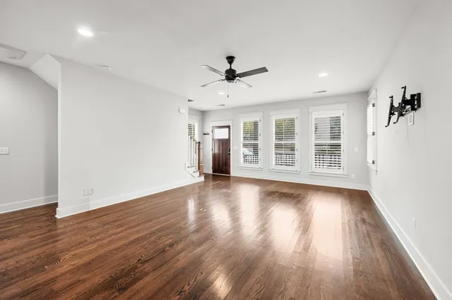 a view of a livingroom with wooden floor a ceiling fan and windows