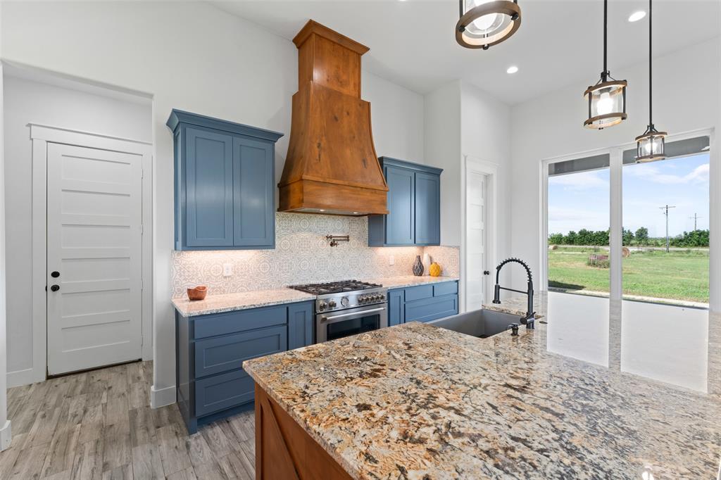 4411 Fm 751 Wills Point Wills Point, TX 75169 - Photo 18 of 40 Kitchen featuring a large central island with granite countertop, blue cabinetry, a wood-finish range hood, stainless steel gas range, and large windows