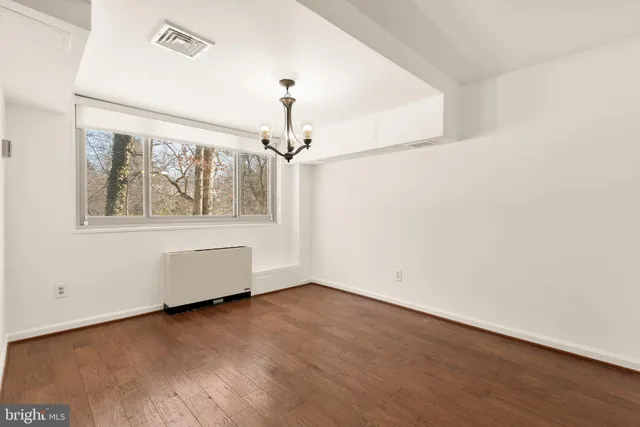 an empty room with wooden floor chandelier and windows