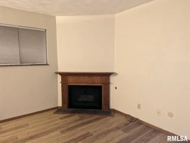 a view of an empty room with wooden floor and a fireplace
