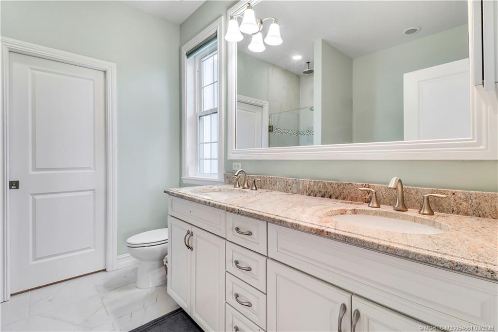 5352 Southeast Nassau Terrace Stuart, FL 34997 - Photo 29 of 53 a bathroom with a granite countertop sink a toilet and a mirror