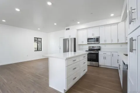 a view of an empty room with wooden floor and a kitchen