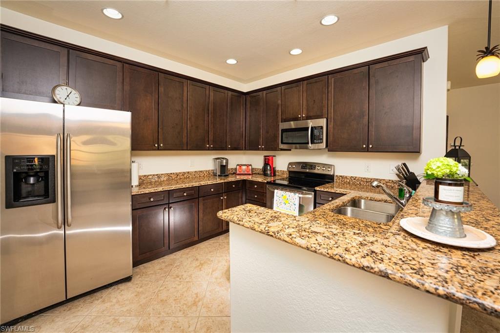 8986 Cambria Circle, Unit 22 Naples, FL 34113 - Photo 7 of 20 Kitchen with light tile patterned floors, light stone countertops, appliances with stainless steel finishes, dark brown cabinetry, and sink