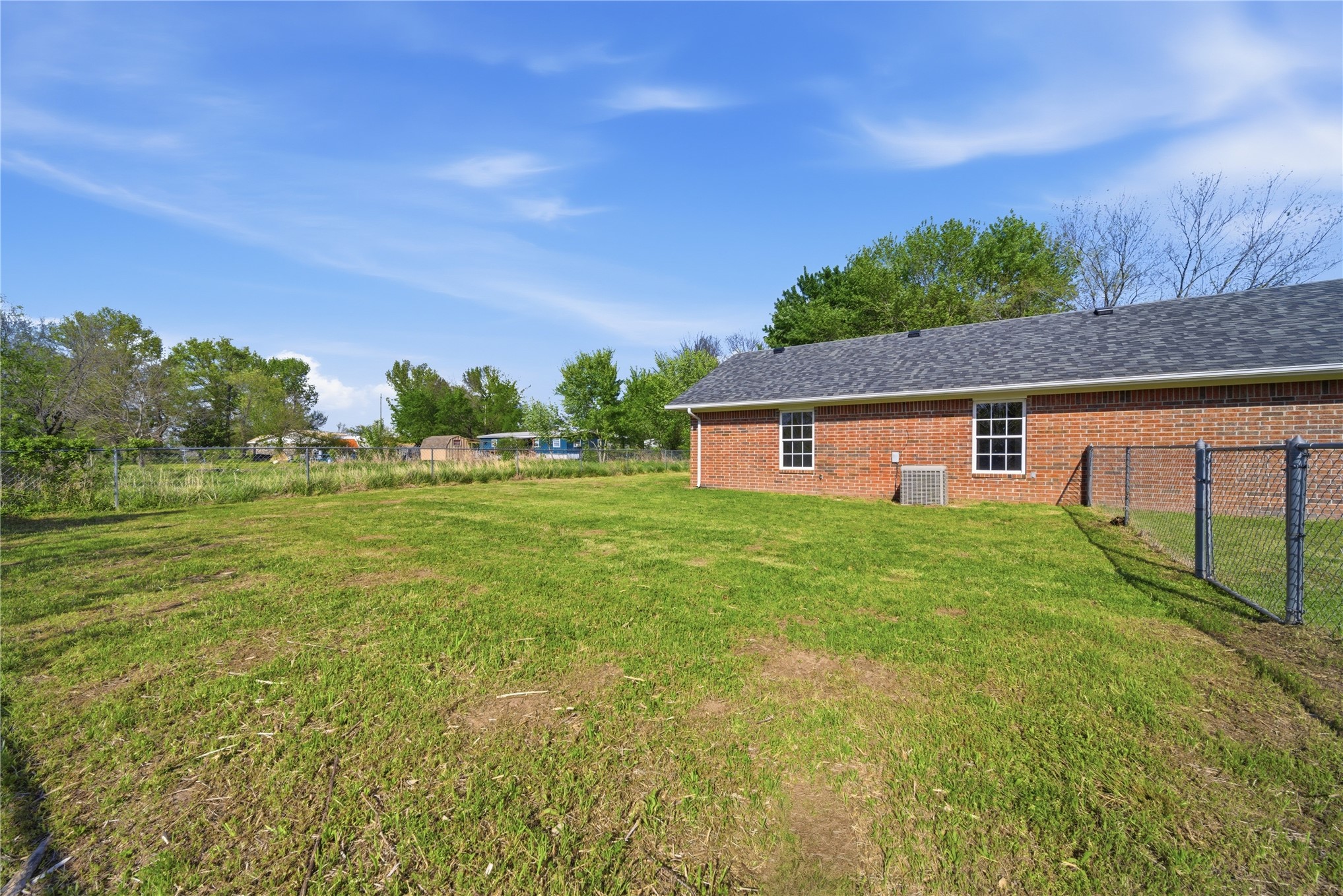 511 Cemetery Road Oktaha, OK 74450 - Photo 27 of 28 Expansive grassy yard with chain-link fencing, featuring a brick exterior and white-framed windows