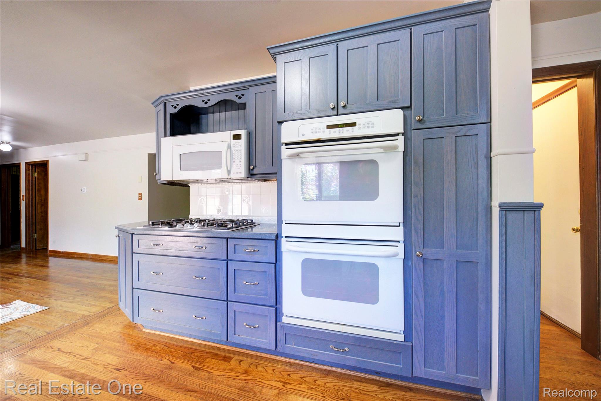 3125 West Commerce Road Milford, MI 48380 - Photo 17 of 63 Kitchen area featuring blue cabinetry, built-in double ovens, a gas cooktop, a microwave, and wood-finish flooring