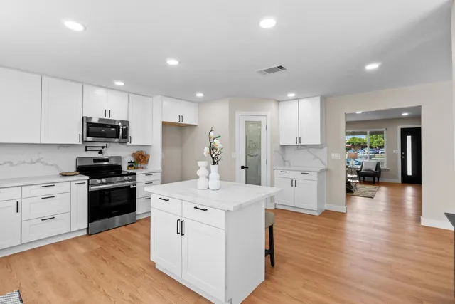 a kitchen with stainless steel appliances kitchen island granite countertop a stove top oven a sink a refrigerator white cabinets and wooden floor
