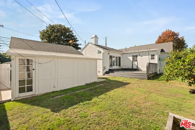 a view of a white house next to a yard with potted plants