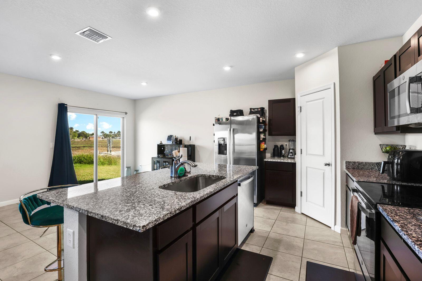 185 Dabou Loop Belle Glade, FL 33430 - Photo 5 of 25 a kitchen with kitchen island granite countertop stainless steel appliances a sink stove and refrigerator