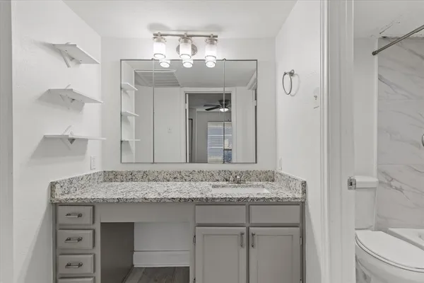 a bathroom with a granite countertop sink a mirror and a toilet