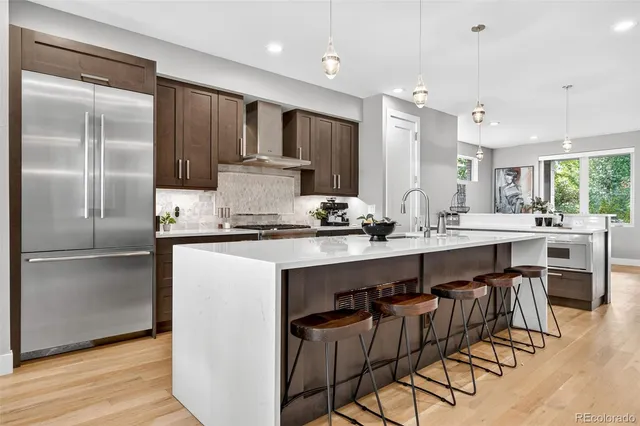 a kitchen with stainless steel appliances kitchen island granite countertop a sink a stove a refrigerator and island with wooden floor