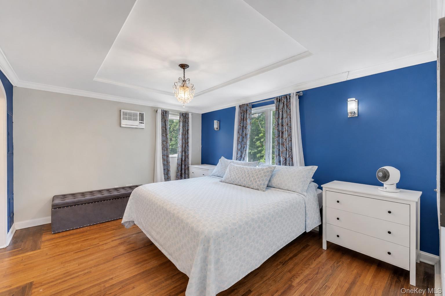 19 Joan Road Bay Shore, NY 11706 - Photo 26 of 50 Bedroom featuring wood-finish flooring, a tray ceiling with a chandelier, crown molding, two windows with curtain rods, and two wall sconces
