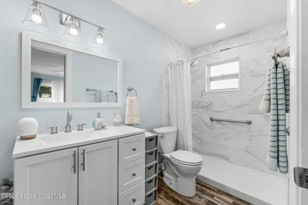 a bathroom with a granite countertop toilet a sink a mirror a shower and vanity