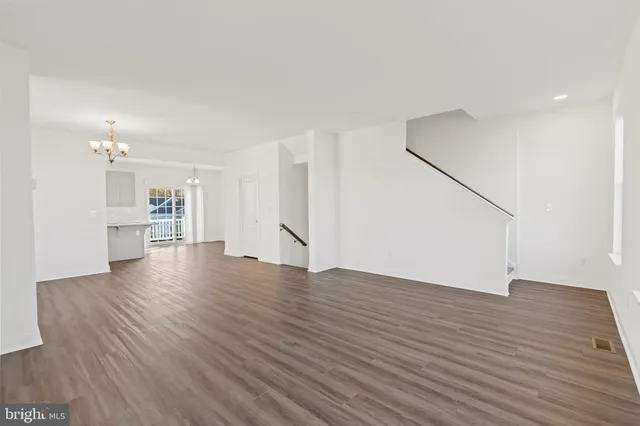 a view of an empty room with wooden floor and a kitchen
