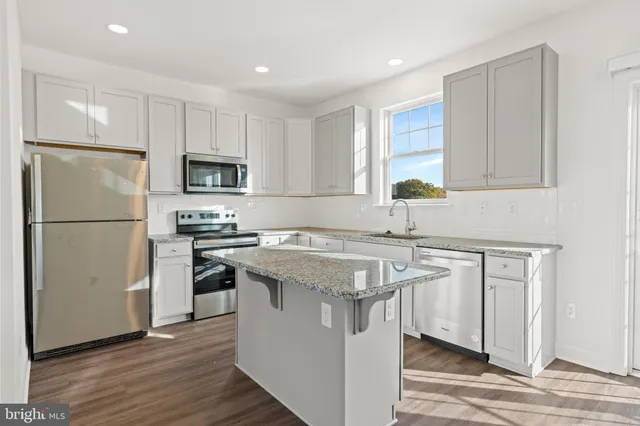 a kitchen with stainless steel appliances granite countertop a refrigerator a sink a stove a microwave and island with wooden floor