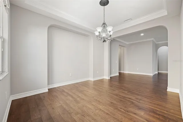 a view of an empty room with wooden floor and chandelier