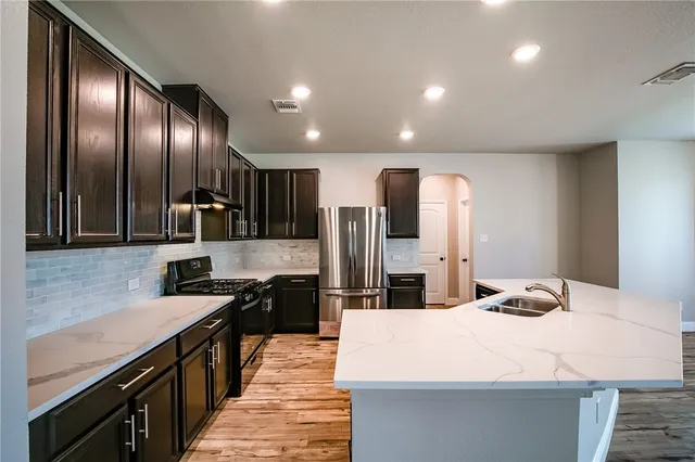 a kitchen with stainless steel appliances kitchen island granite countertop a refrigerator a stove and a sink with wooden floor