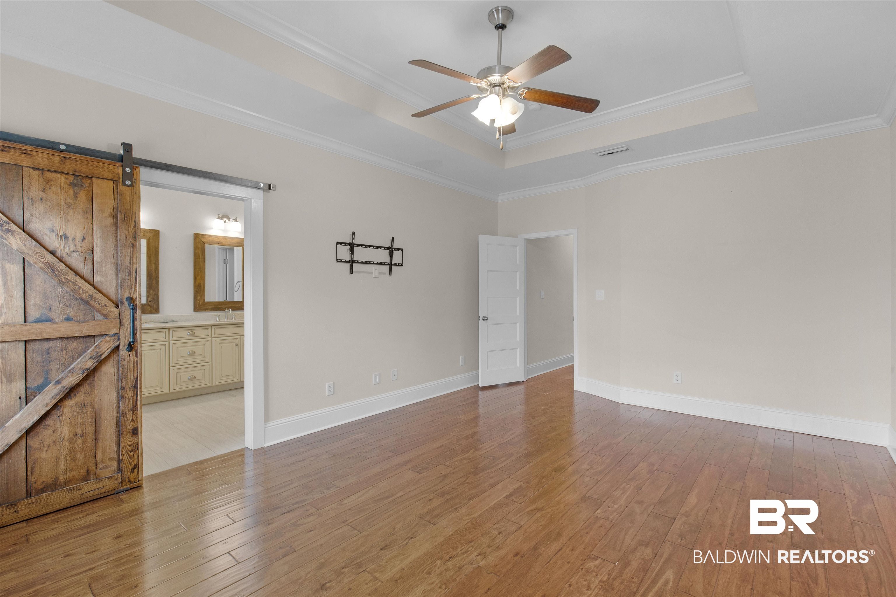 25092 Fairfax Road Daphne, AL 36526 - Photo 22 of 29 Empty room featuring crown molding, light hardwood / wood-style floors, a barn door, and a raised ceiling