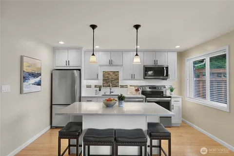 a kitchen with stainless steel appliances a refrigerator a stove a dining table and chairs with wooden floor