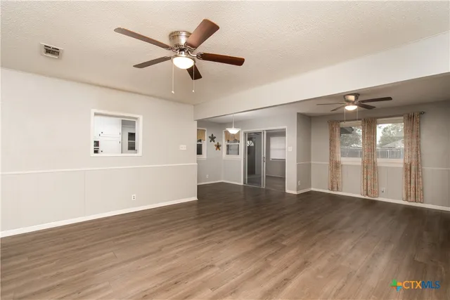 a view of an empty room with wooden floor and a ceiling fan
