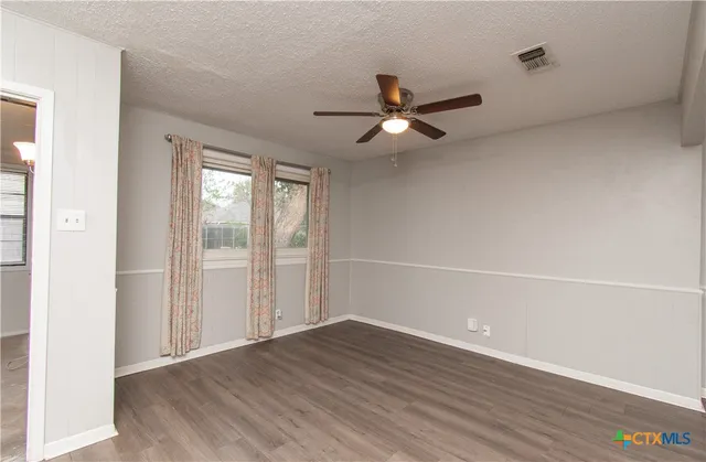 an empty room with wooden floor fan and windows