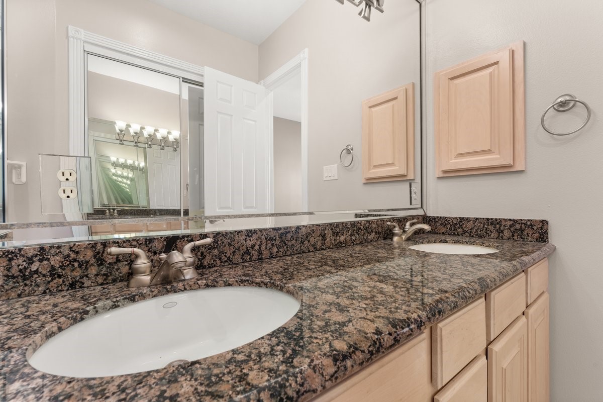 168 Lake Point Boulevard, Unit C102 Conroe, TX 77356 - Photo 22 of 35 This bathroom features a dual-sink vanity with elegant granite countertops, light wood cabinetry, and a large mirror, offering a spacious and modern feel.