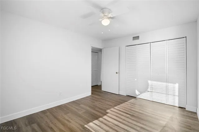 a view of an empty room with wooden floor and a ceiling fan