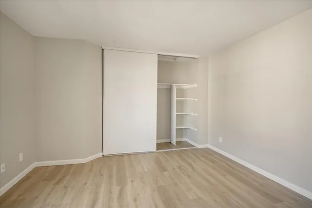 a view of an empty room with wooden floor and closet