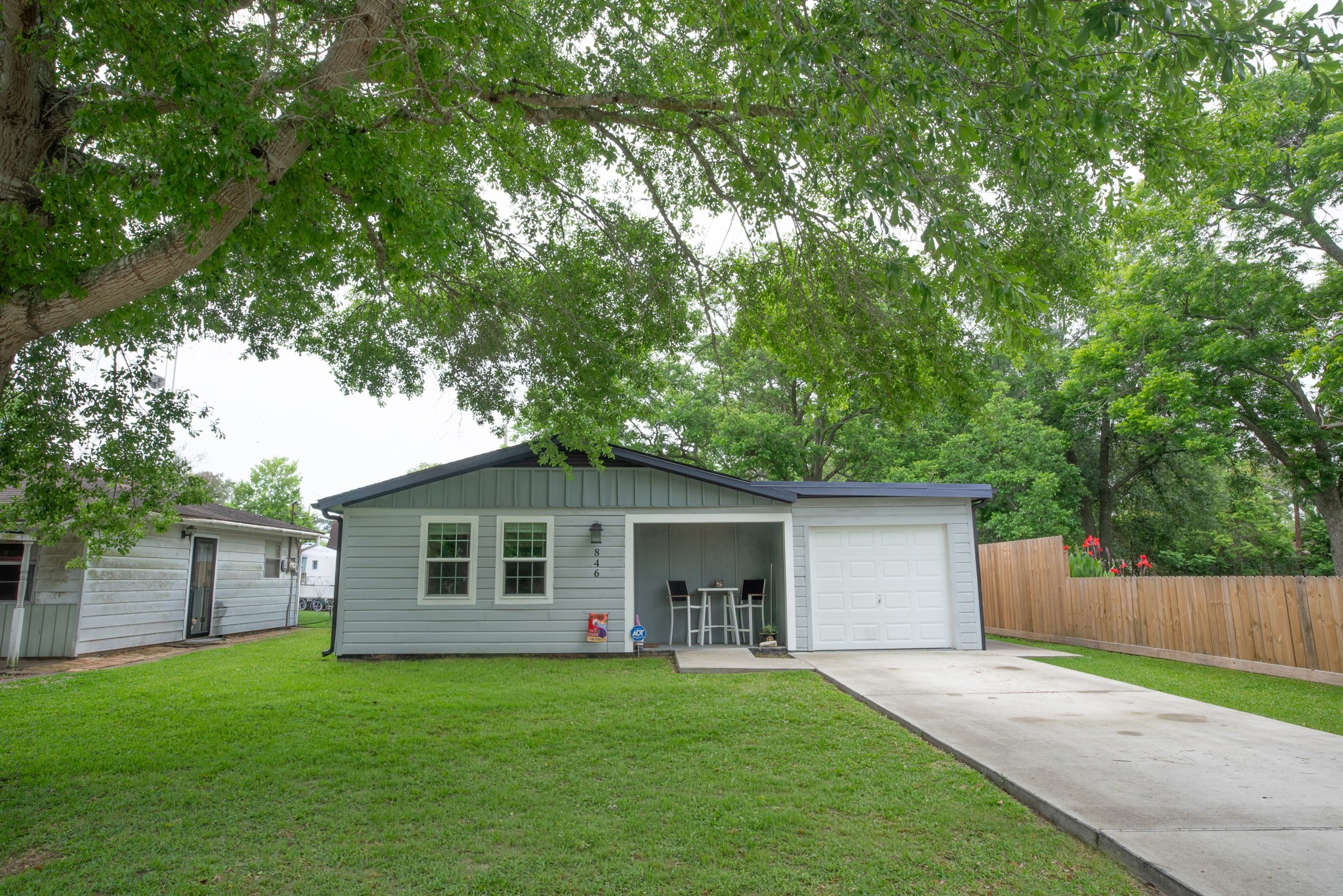 846 South Anderson Street Angleton, TX 77515 - Photo 4 of 30 Charming single-story home with gray siding, featuring a cozy front porch and an attached converted garage. The property has a lush green lawn and is surrounded by mature trees, offering privacy with a wooden fence.