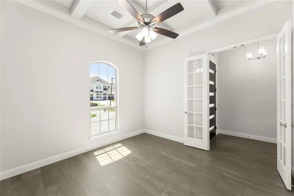 an empty room with wooden floor chandelier fan and windows