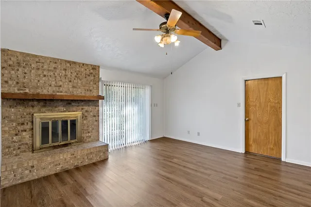 an empty room with wooden floor fireplace and windows
