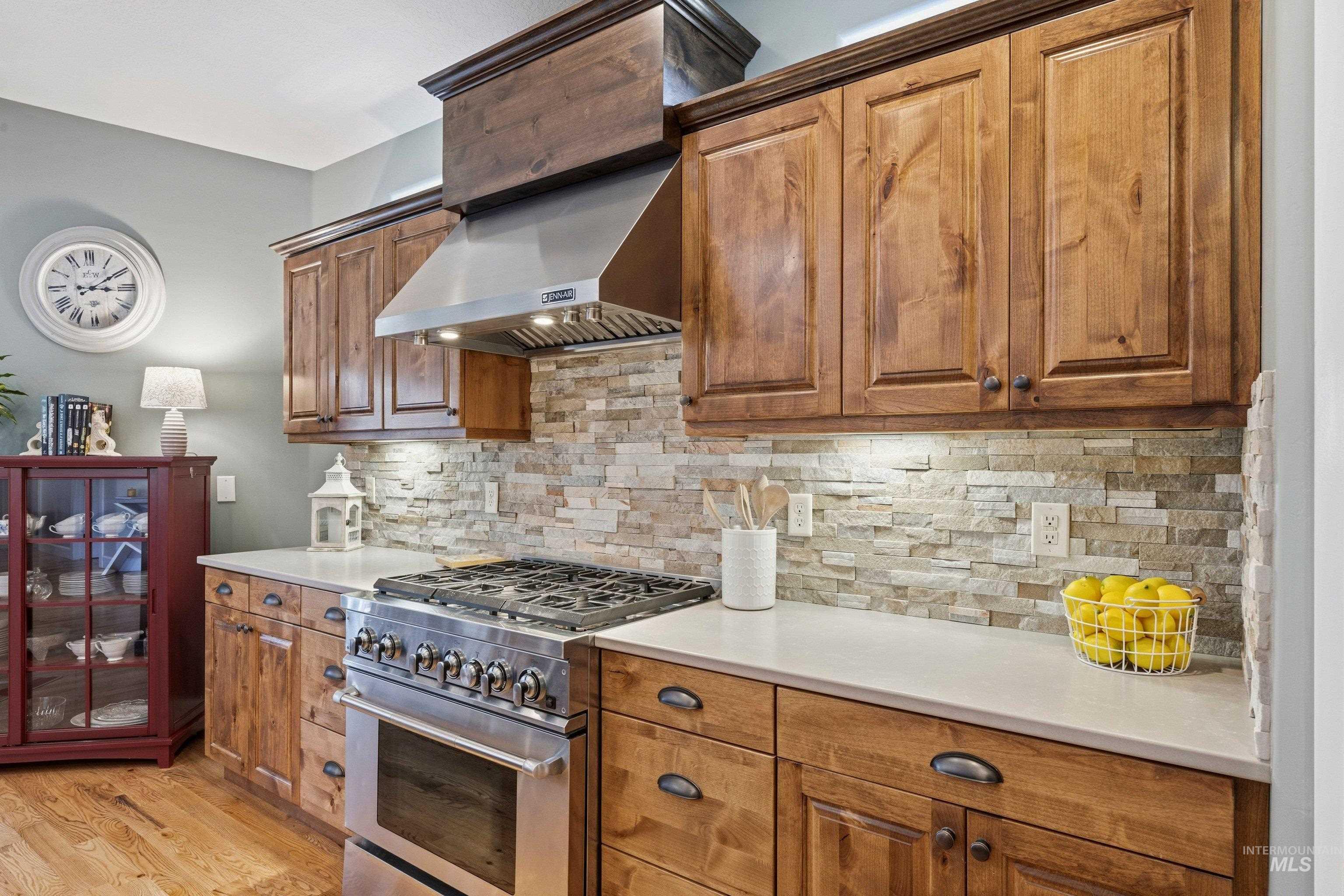 5850 North Rio Lomas Avenue Meridian, ID 83646 - Photo 12 of 50 Kitchen with stainless steel stove, wood finish cabinets, tasteful backsplash, light wood-style floors, and light stone countertops