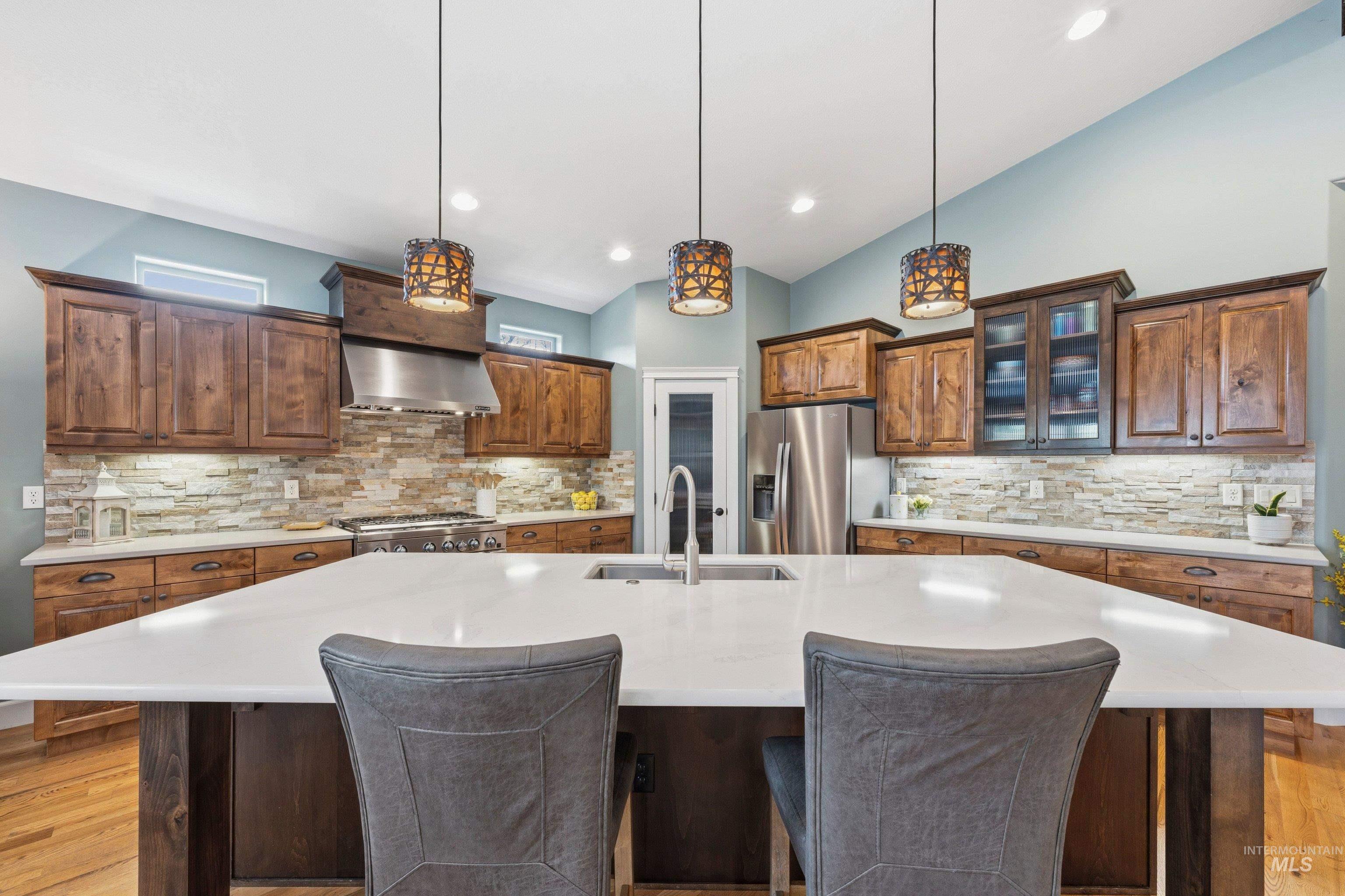 5850 North Rio Lomas Avenue Meridian, ID 83646 - Photo 14 of 50 Kitchen with light wood-style floors, backsplash, lofted ceiling, glass fronted cabinets, and a large island with sink