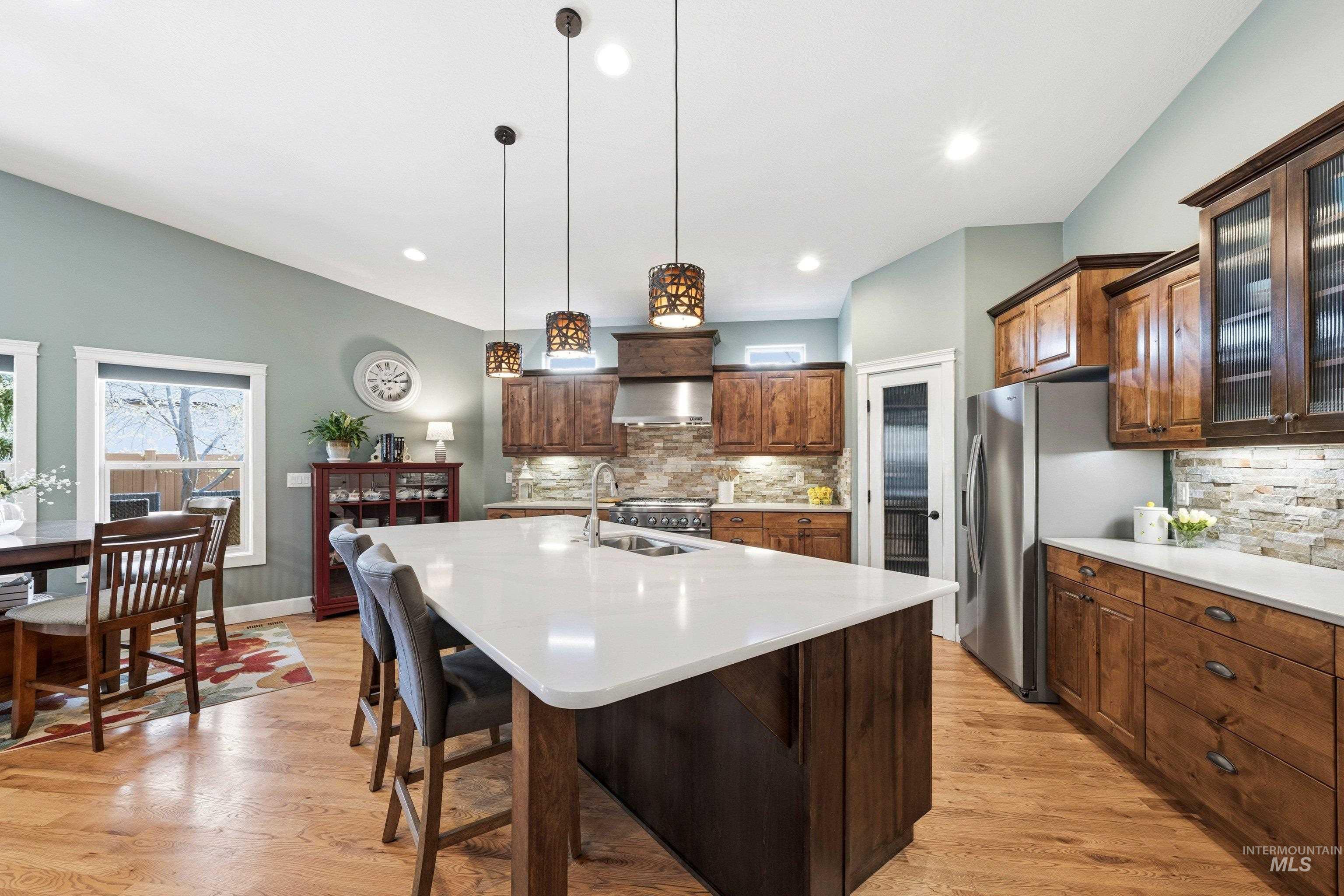 5850 North Rio Lomas Avenue Meridian, ID 83646 - Photo 9 of 50 Kitchen featuring glass insert cabinets, an island with sink, stainless steel appliances, light wood-style floors, and decorative backsplash