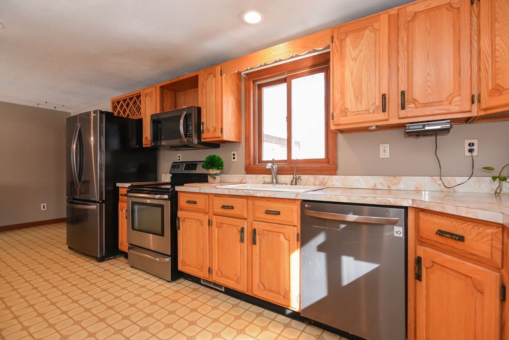 73 Drew Road Derry, NH 03038 - Photo 11 of 42 a kitchen with stainless steel appliances granite countertop a stove a sink dishwasher and a refrigerator with wooden cabinets