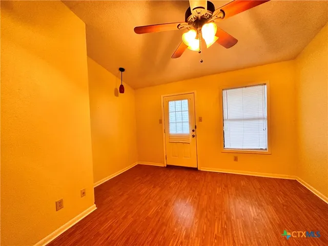 a view of an empty room with wooden floor and a ceiling fan