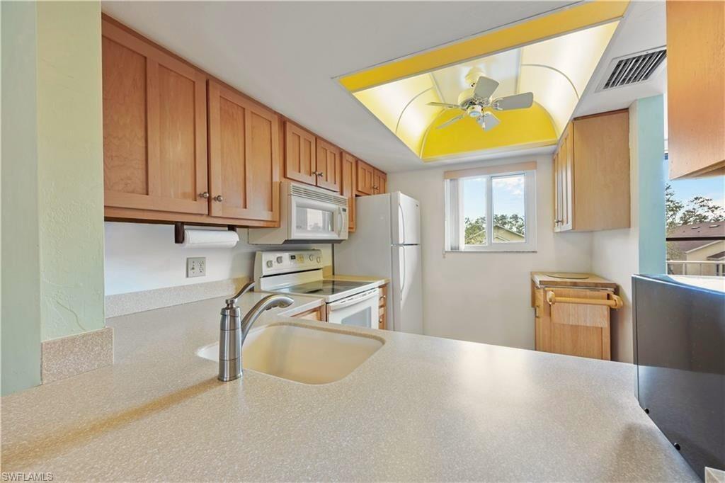 1018 Manatee Road, Unit E302 Naples, FL 34114 - Photo 6 of 19 Kitchen featuring white appliances, ceiling fan, light countertops, and brown cabinetry