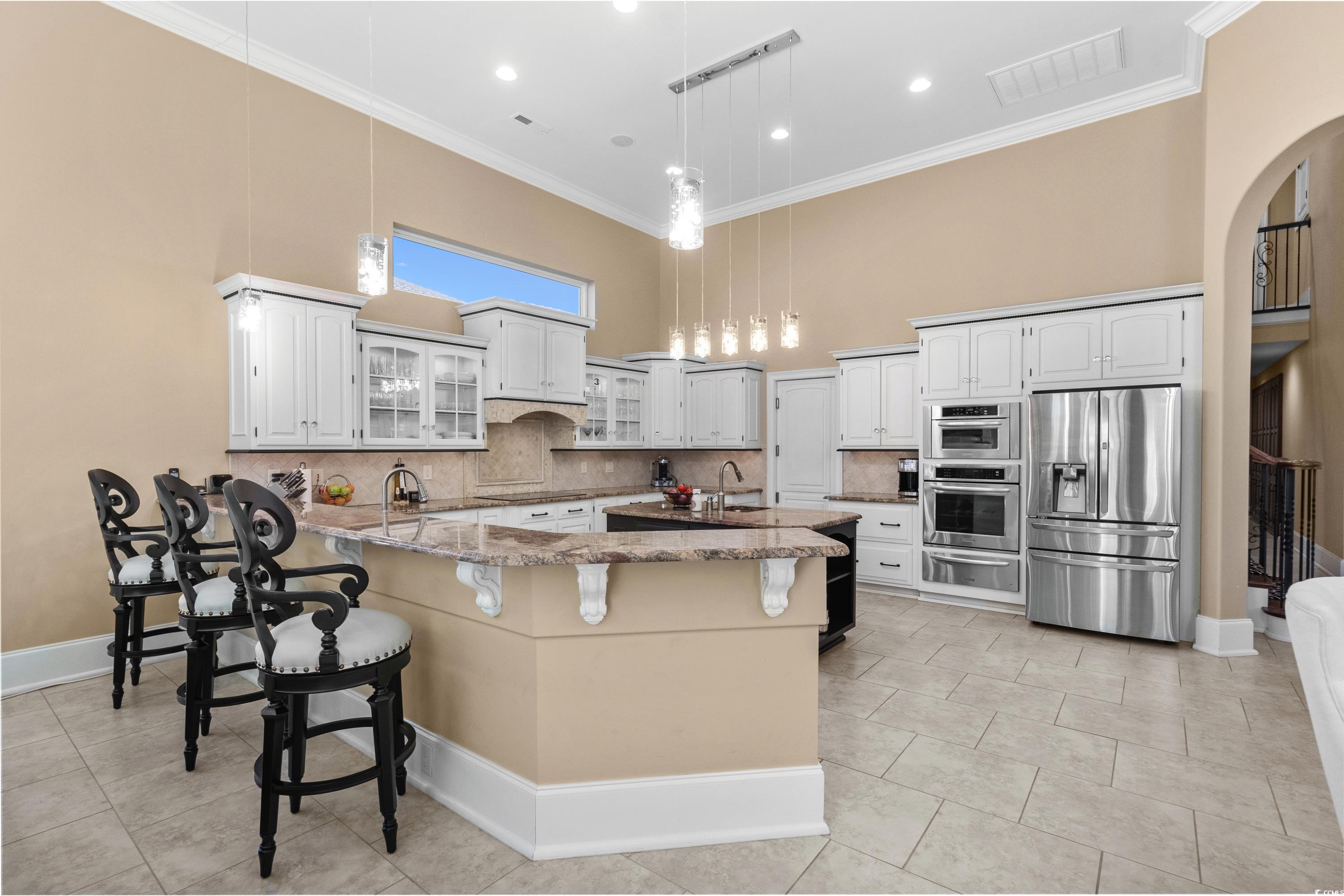 9237 Bellasera Circle Myrtle Beach, SC 29579 - Photo 13 of 34 Kitchen with stainless steel fridge, a warming drawer, a peninsula, light stone counters, and a breakfast bar area