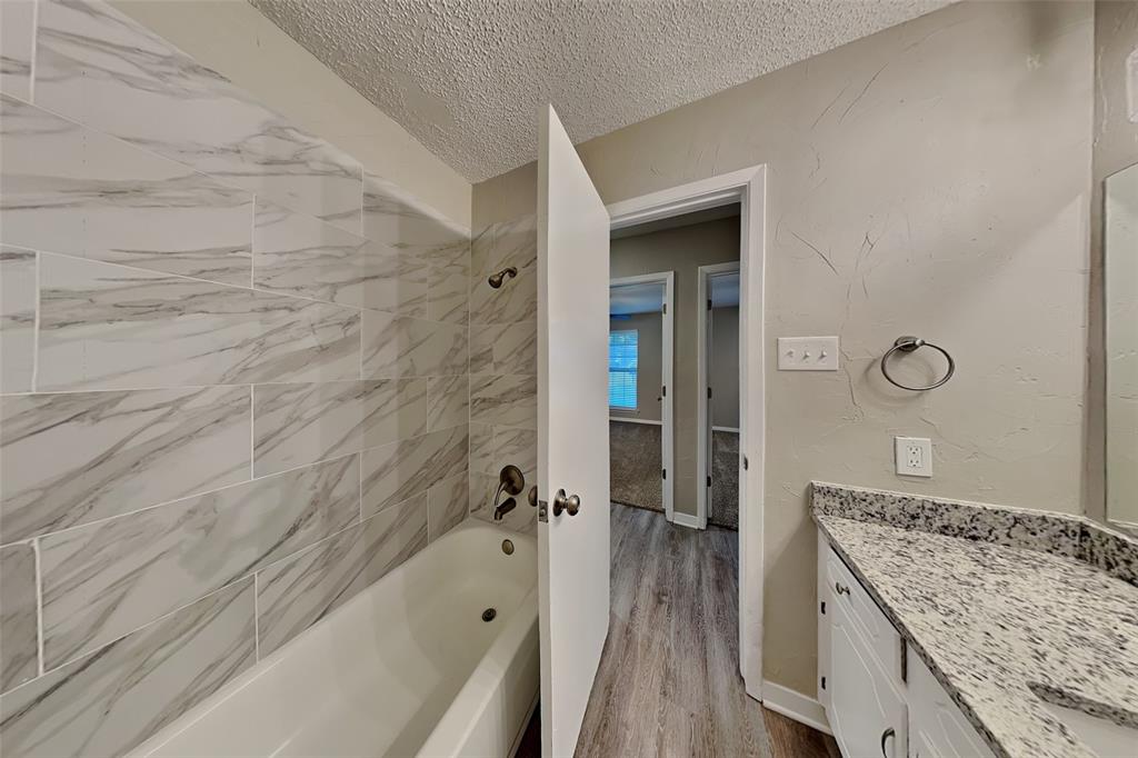 6432 Ridglea Drive Watauga, TX 76148 - Photo 16 of 18 Full bathroom with a textured ceiling, shower / bathtub combination, vanity, light wood-type flooring, and a textured wall
