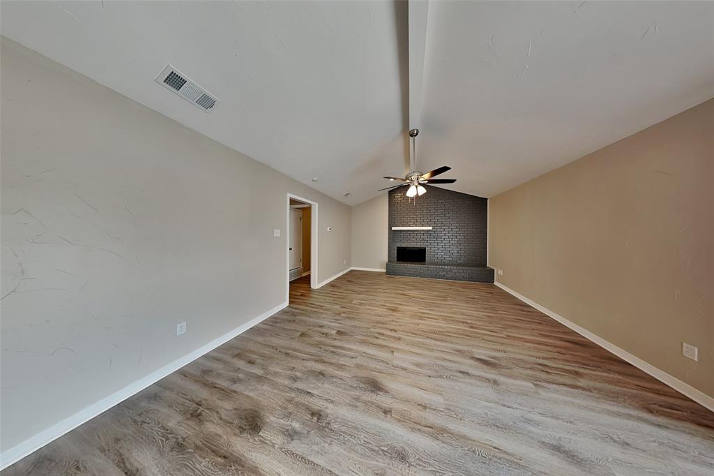 6432 Ridglea Drive Watauga, TX 76148 - Photo 2 of 18 Unfurnished living room featuring vaulted ceiling, a ceiling fan, a fireplace, and light wood-type flooring