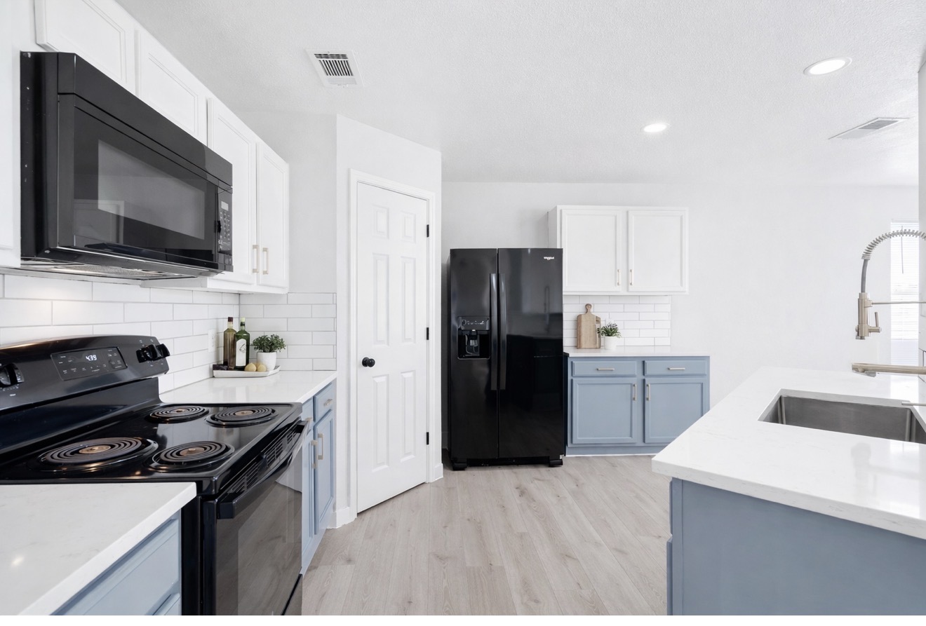 313 Drystone Trail Liberty Hill, TX 78642 - Photo 6 of 17 Kitchen with black appliances, two tone cabinets, light wood-style flooring, light stone counters, and recessed lighting