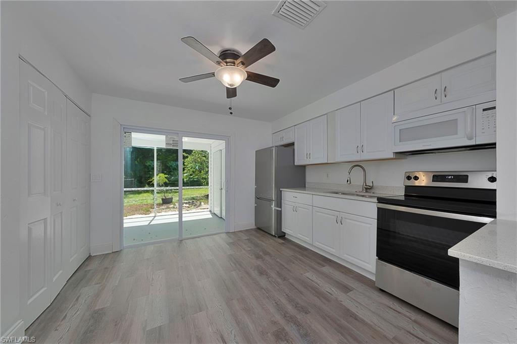 19133 Tangerine Road Fort Myers, FL 33967 - Photo 13 of 17 Kitchen with appliances with stainless steel finishes, light hardwood / wood-style flooring, light stone countertops, white cabinetry, and ceiling fan