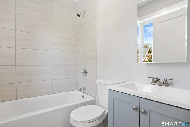 a bathroom with a bathtub shower sink vanity mirror and toilet