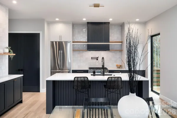 a kitchen with stainless steel appliances kitchen island granite countertop a refrigerator a stove a sink and white cabinets with wooden floor